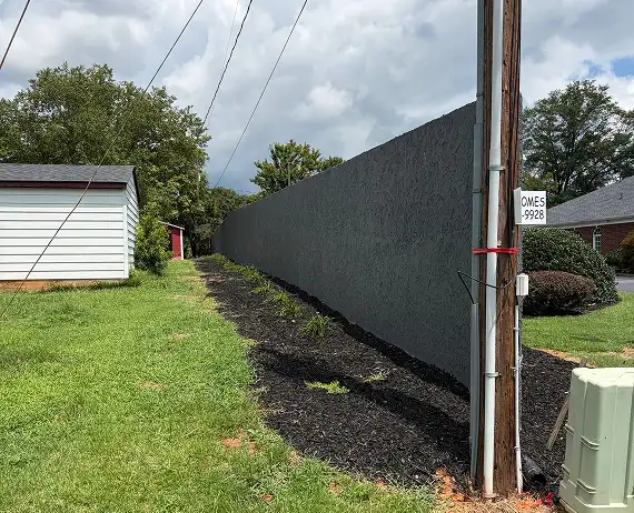 Modern tall charcoal grey stucco privacy wall with black mulch landscaping