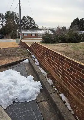 Low red brick boundary wall beside driveway with pile of melting snow